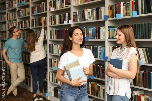 Young people standing near bookshelves in library