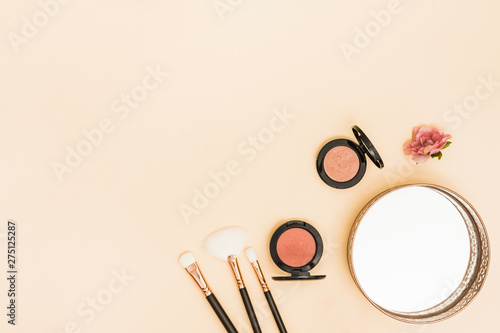 Makeup brushes; compact face powder; rose and mirror on the corner of colored backdrop