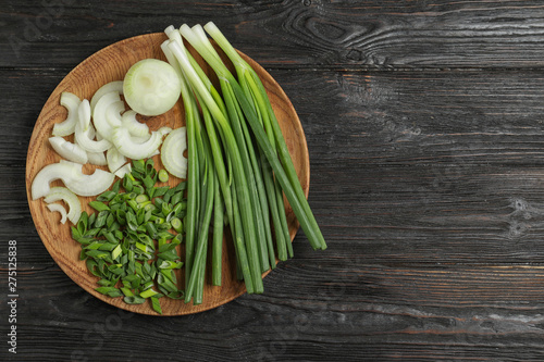 Wooden plate with cut onion leaves and bulbs on dark wooden table, top view. Space for text