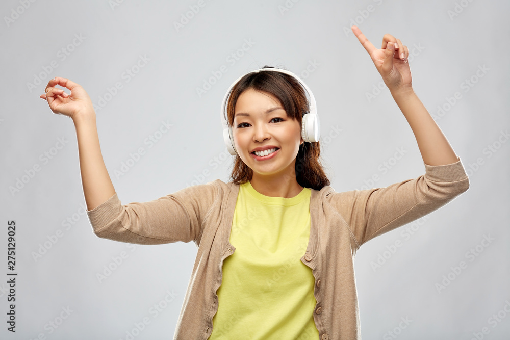 people, technology and audio equipment concept - happy young asian woman in headphones listening to music and dancing over grey background people, technology and audio equipment concept - happy young asian woman in headphones listening to music and dancing over grey background