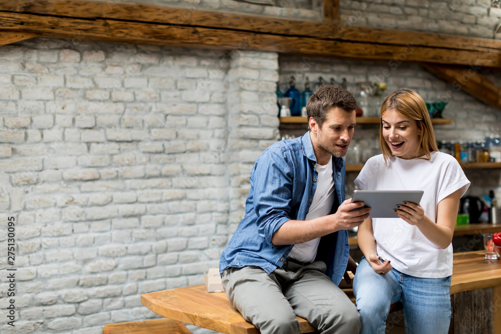Young couple using a digital tablet and smiling while sitting on the table at home Young couple using a digital tablet and smiling while sitting on the table at home