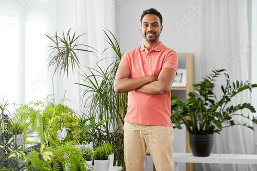 people, nature and plants concept - smiling indian man with houseplants at home
