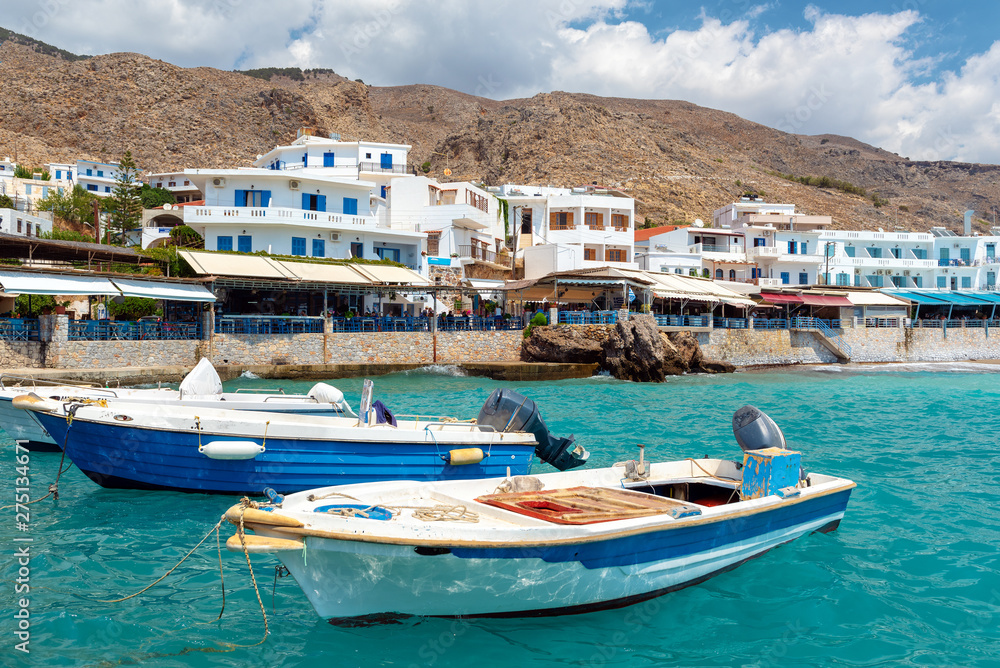Small moored fishing boats in blue lagoon of Crete island.