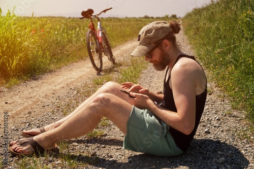 Modern man sitting on a dusty road with his bike lokin at phone photo
