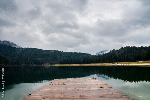 Fototapeta Naklejka Na Ścianę i Meble -  Montenegro, Wooden landing stage on calm perfect glassy lake water of black lake in durmitor national park nature landscape in the evening