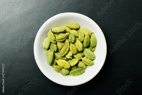 Top view of cardamom in white bowl on black textured background