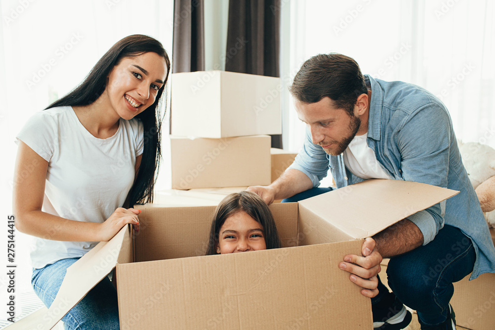 Happy family having fun while moving into new apartment. Mother, father and daughter together smiling, with Cardboard boxes on background Happy family having fun while moving into new apartment. Mother, father and daughter together smiling, with Cardboard boxes on background