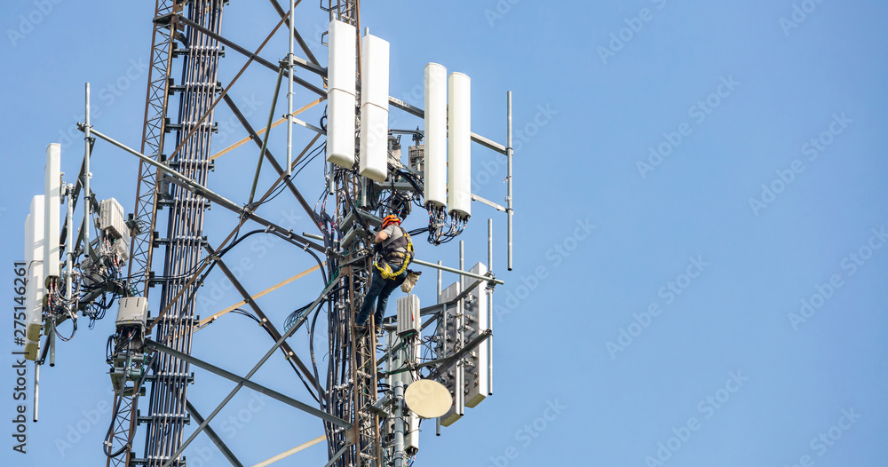 Telecom maintenance. Man climber on tower against blue sky background - obrazy, fototapety, plakaty 