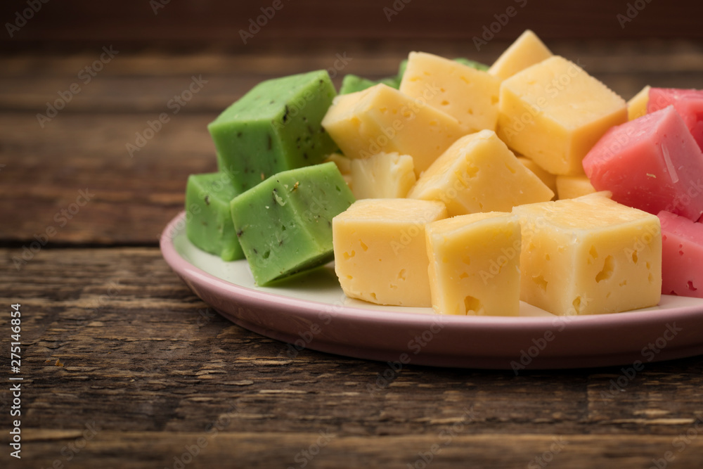 Set of multicolored cheese on a plate, wooden background. Wine appetizer. Copy space