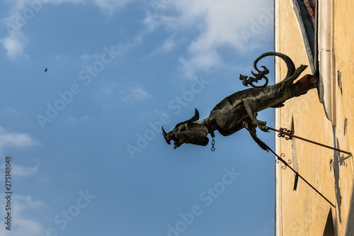 An old drainpipe in the shape of a dragon on the wall of an old house against the background of a blue sky with a bird soaring in height.