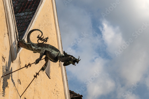 Ancient drainpipe in the form of a dragon on the roof of an old house against the background of a cloudy sky.