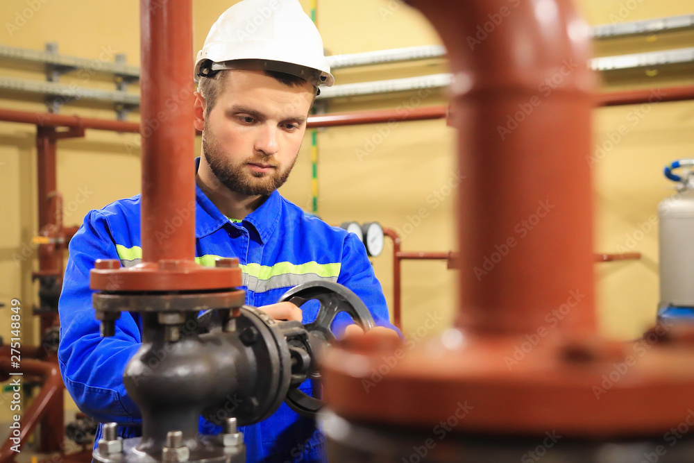 Technician worker on heating system. Station operator opens water valve on pipeline. Man works on industrial boiler