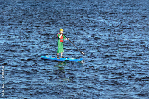 Woman on stand up paddle board. slim girl in a yellow helmet and a long green dress floating on the river on the SUP board