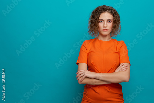 Serious model in orange dress with crossed hands.