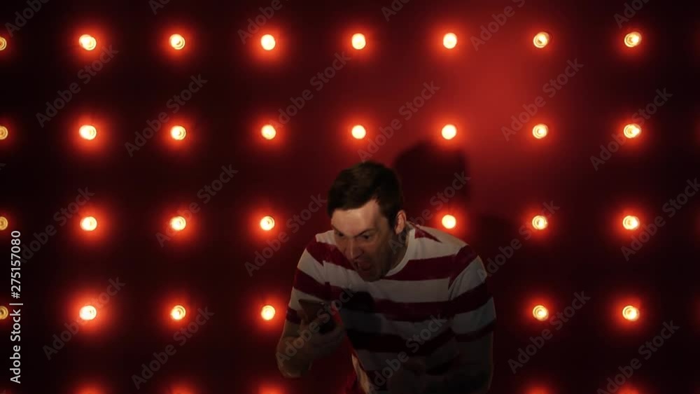 Happy young man standing by a lit wall using smartphone. Concept: happy or good news Happy young man standing by a lit wall using smartphone. Concept: happy or good news