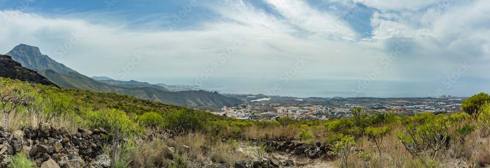 Stony path at upland surrounded by endemic plants. Sunny day. Clear blue sky and some clouds along the horizon line. Rocky tracking road in dry mountain area. Tenerife. Wide angle panorama