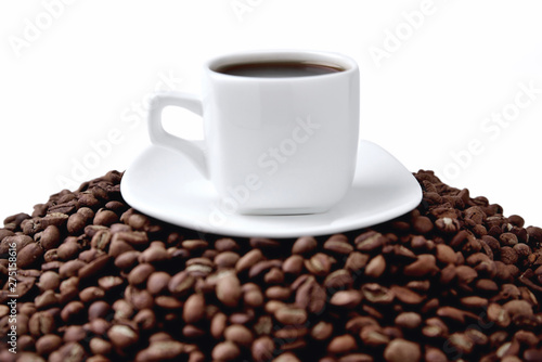 white cup of coffee on a white saucer stands on a hill of coffee beans on a white background