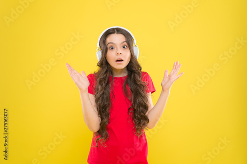 Hear it and live it. Adorable headset user on yellow background. Small child wearing adjustable white headset. Little girl using wireless headset. Cute kid listening to music in stereo headset