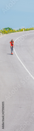 Male caucasian longboarder riding downhill on an empty road, preparing for a speed tuck on the next turn he has to make. Wearing a red t-shirt green hat and black jeans.