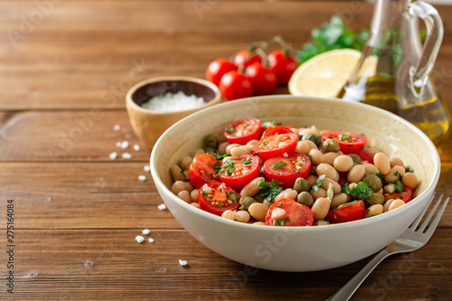 White bean salad with tomatoes, capers, garlic and parsley in bowl on wooden table. Selective focus.