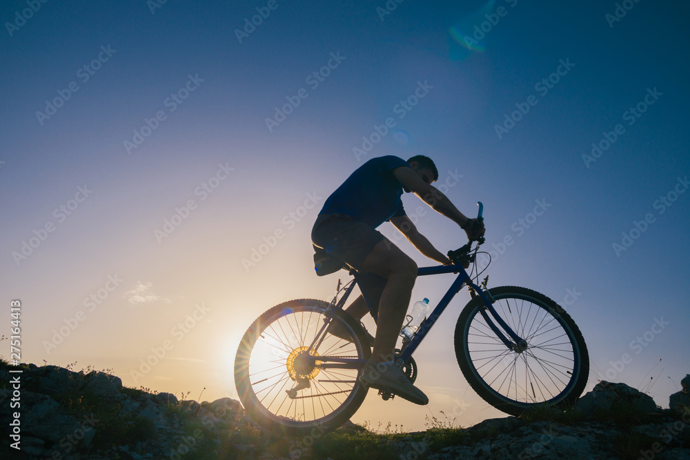 Silhouette of a fit male mountain biker riding his bike uphill on rocky harsh terrain on a sunset. Silhouette of a fit male mountain biker riding his bike uphill on rocky harsh terrain on a sunset.