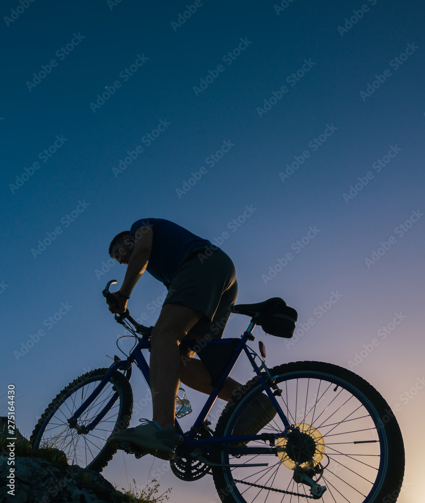 Silhouette of a fit male mountain biker riding his bike uphill on rocky harsh terrain on a sunset. Silhouette of a fit male mountain biker riding his bike uphill on rocky harsh terrain on a sunset.