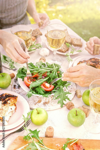 People eat in the garden at the table. Dinner concept with wine in the fresh air. Grilled sea fish and salads with vegetables and herbs. Mediterranean Kitchen. Vertical shot