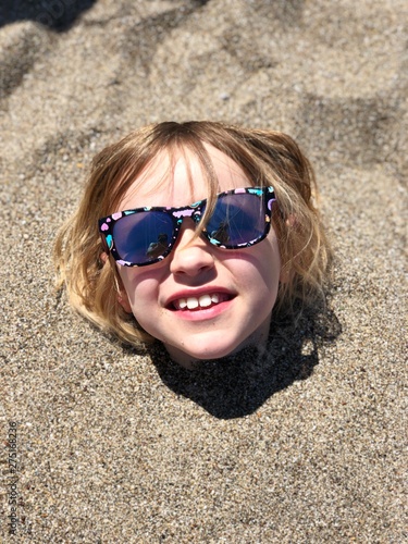 Child playing joy summertime sunglasses buried sand beachday