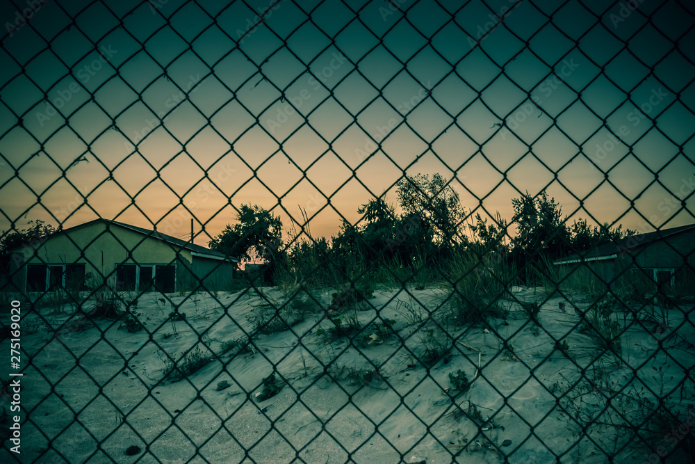Old houses of an abandoned city behind a metal mesh fence Old houses of an abandoned city behind a metal mesh fence
