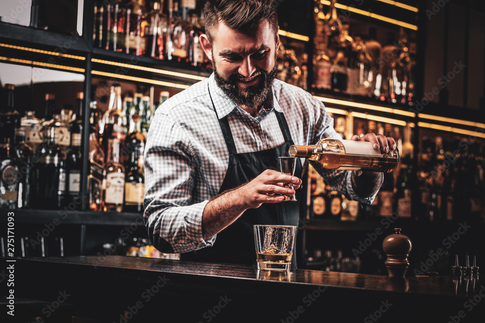 Diligent happy barman is preparing alcoholic beverege for customer.
