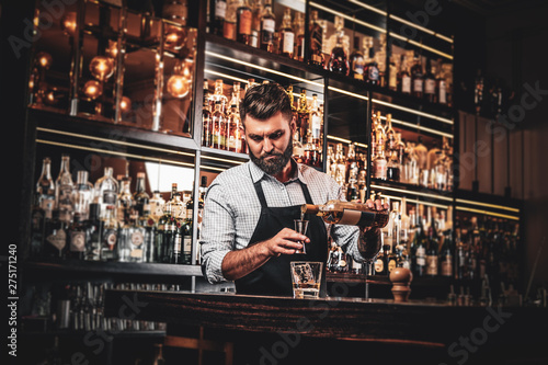 Serious barman is prepairing drinks for customers at posh bar.
