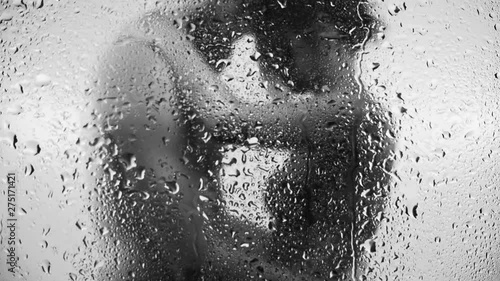 Heterosexual couple hugging each over, black and white, focus on drops of water on glass