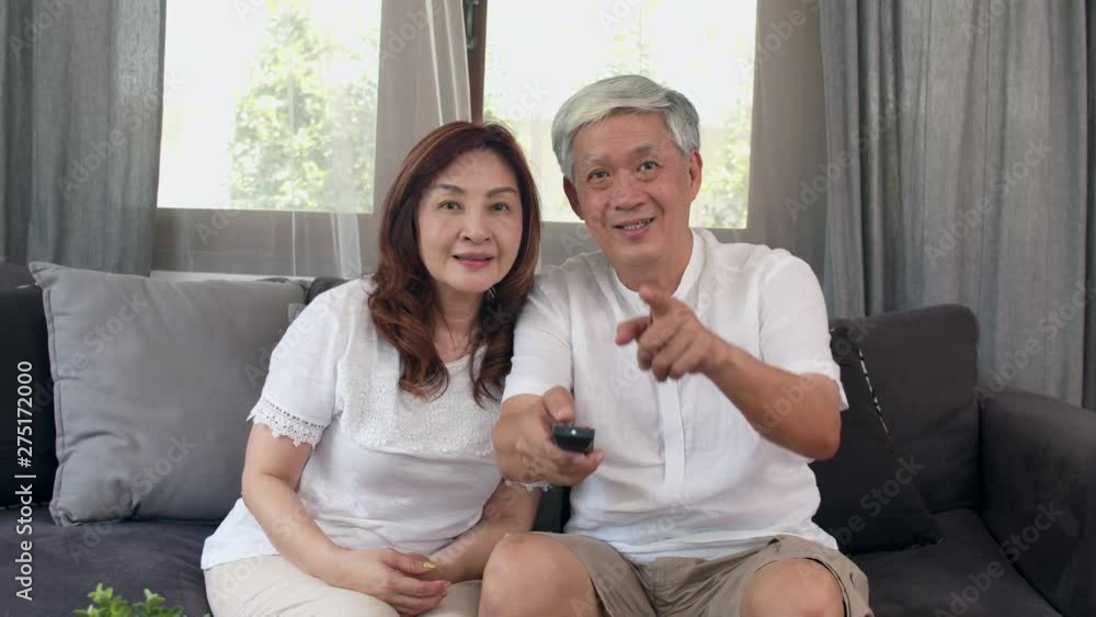 Asian elderly couple watching television in living room at home, Asia couple enjoy love moment while lying on the sofa when relaxed at house. Enjoying time lifestyle senior family concept. Slow motion