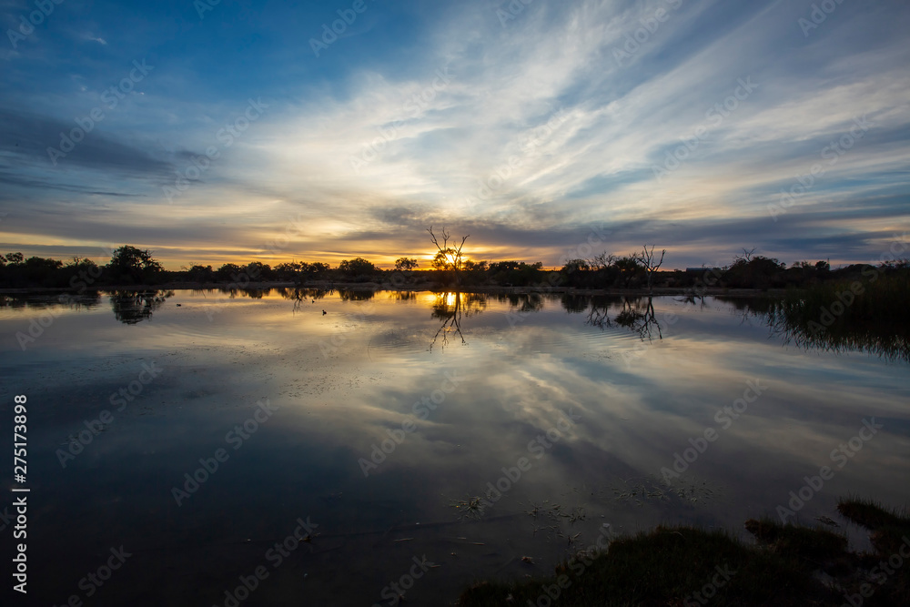 Dramatic sky, trees in silhouette and reflections on water at dusk in the Australian Outback