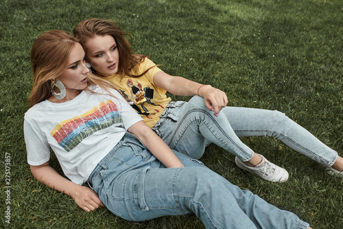 Two happy young woman having fun on the grass wearing trendy shirts and jeans. Youth and happiness concept.