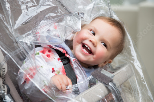 Baby girl in stroller playing with rain coat