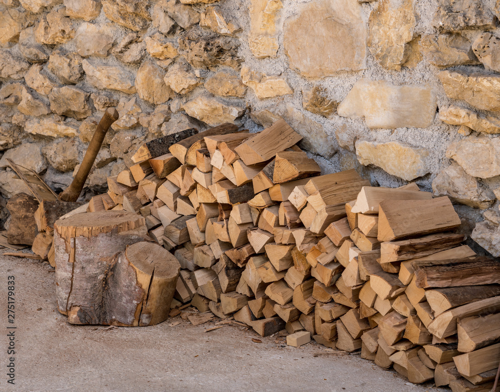 Chopped wood and axe stacked against the stone wall of a rustic farmhouse Chopped wood and axe stacked against the stone wall of a rustic farmhouse