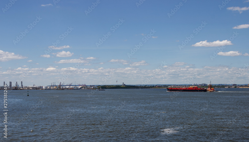 An orange vessel transports people to islands in New Jersey. Against the backdrop of the distance are the skyscrapers of New York, Manhattan.