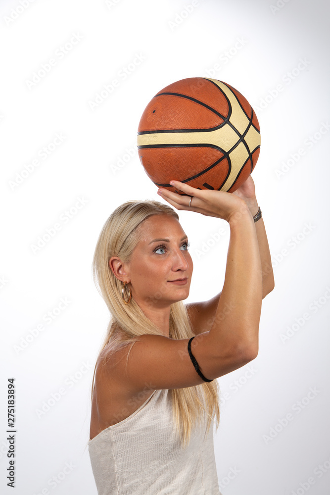 A beautiful young Caucasian woman is viewed playing basketball. Isolated against a white background, she holds the ball ready to score in a net.