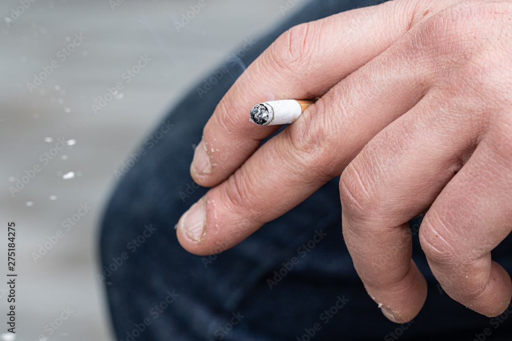 A closeup view of a smoking cigarette in the hand of a Caucasian person. Bad health and carcinogenic concept.