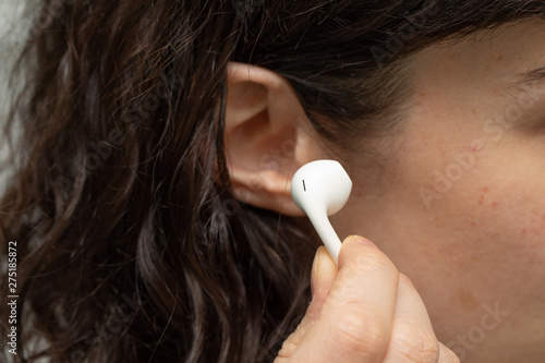 A close-up view of a young lady placing an earphone into her ear. Music and lifestyle concept.