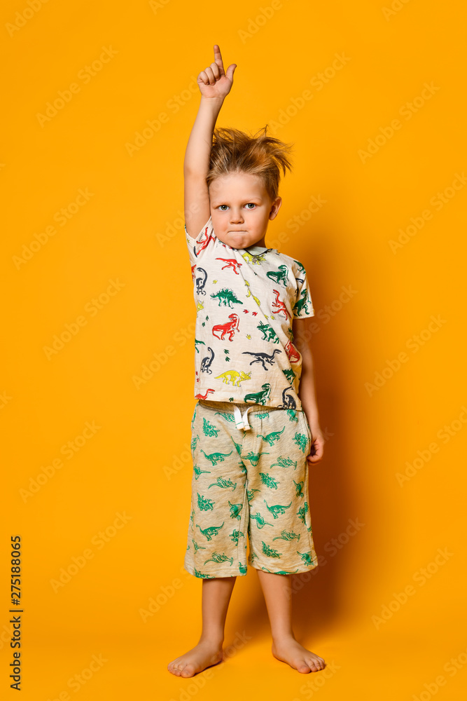 Little cute blond boy preschooler in pajamas with dinosaurs having fun has joy in the studio over yellow background. Little cute blond boy preschooler in pajamas with dinosaurs having fun has joy in the studio over yellow background.