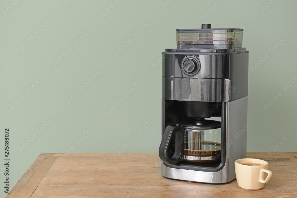 Modern coffee machine and cup on table against color background Modern coffee machine and cup on table against color background