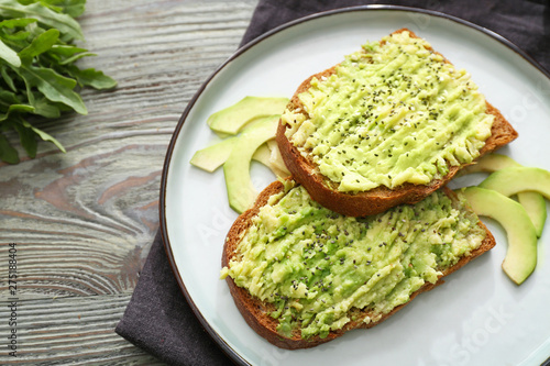 Plate with tasty avocado toasts on wooden table
