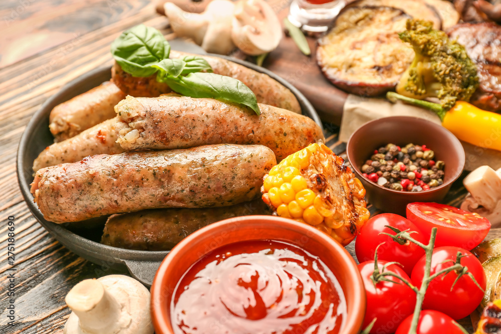 Frying pan with tasty grilled sausages and vegetables on wooden table