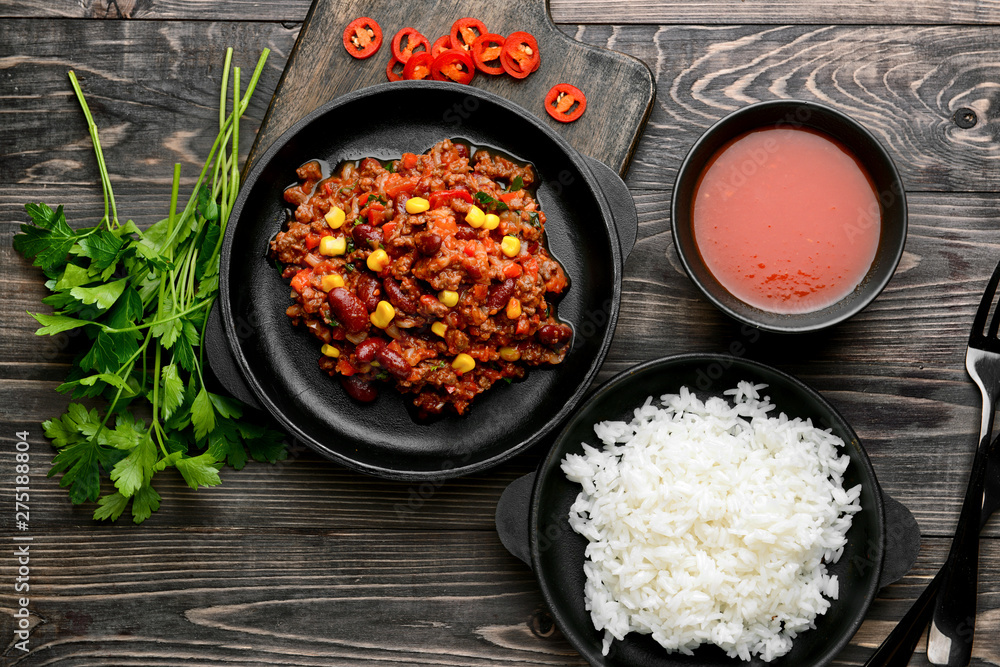 Frying pans with tasty chili con carne and rice on wooden table Frying pans with tasty chili con carne and rice on wooden table