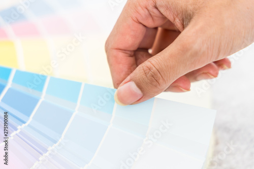 Hand of woman designer choosing interior design color from swatch palette. Color palette, guide of paint samples, colored catalog.