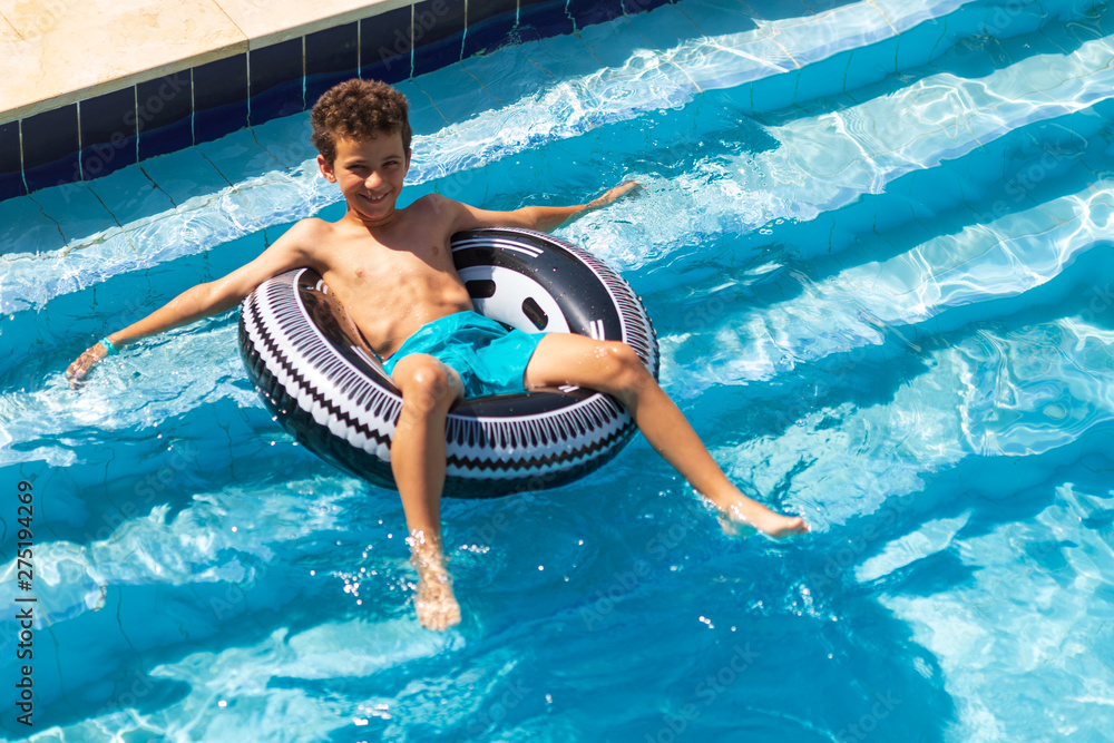 Boy floating on an inflatable black circle in the pool. closes eyes from bright sunshine