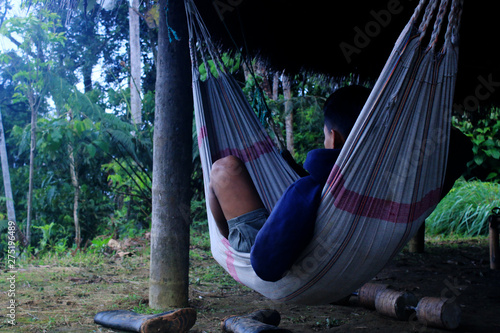 A hispanic person laying in a white hammock under a roof of leaves