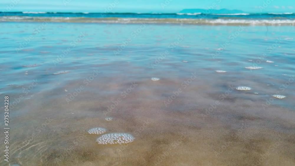 Close Up: Turquoise ocean waves roll in on the peaceful shore with sea birds in the background. View of swell reaching sandy beach. Close Up: Turquoise ocean waves roll in on the peaceful shore with sea birds in the background. View of swell reaching sandy beach.
